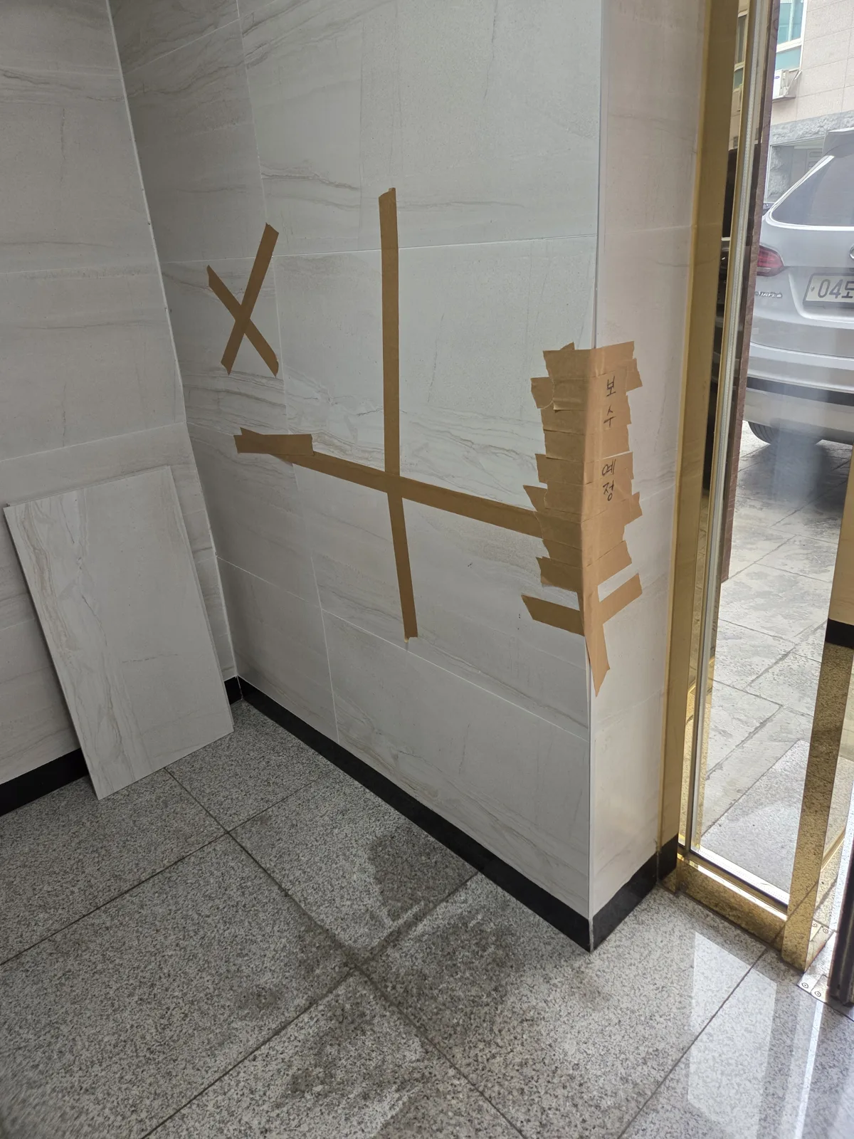 타일 벽 구멍 메우기·복원 — 보수할 자리를 테이프로 표시한 타일 벽